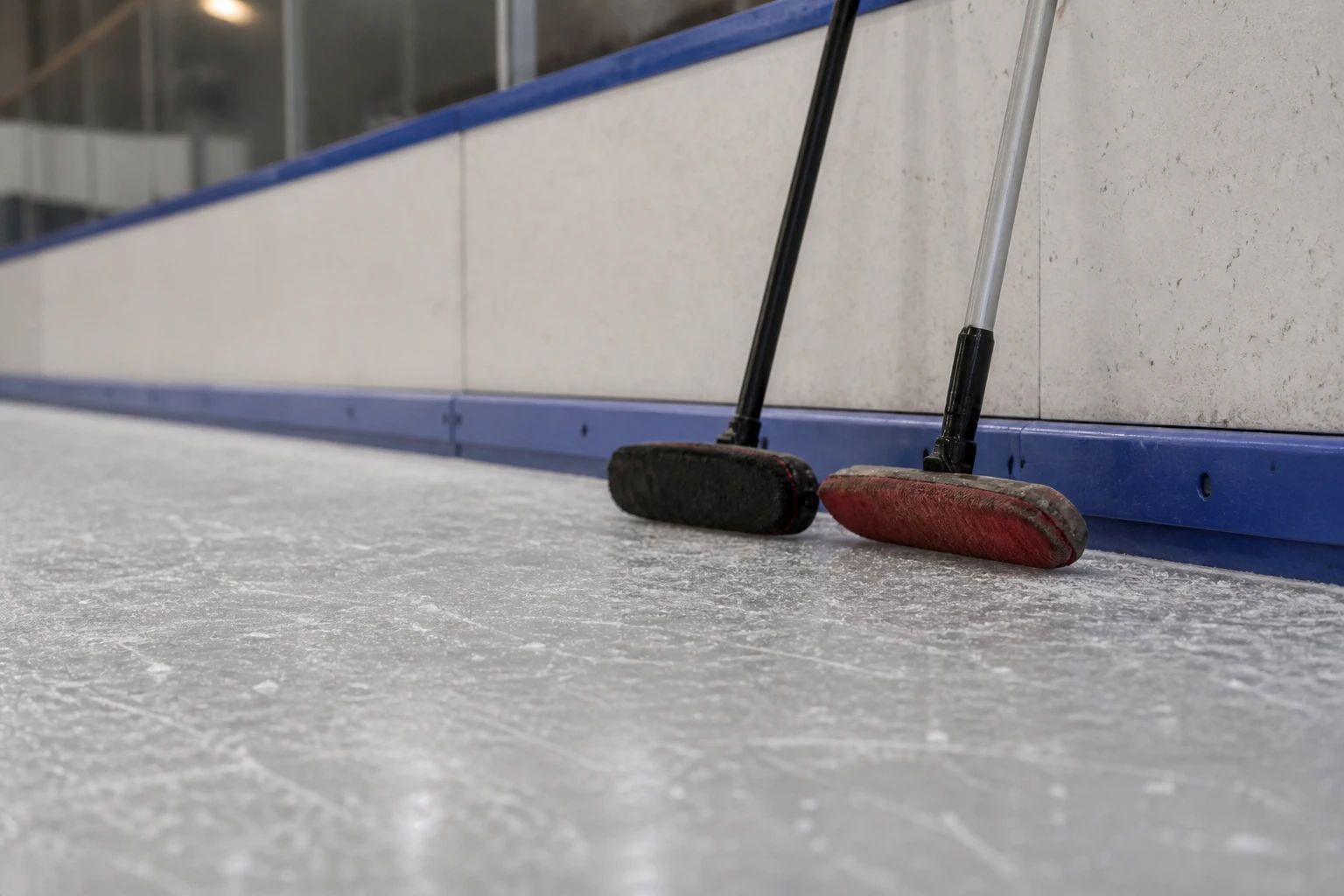 Två curlingborstar lutade mot sargen ovanför pebblad is