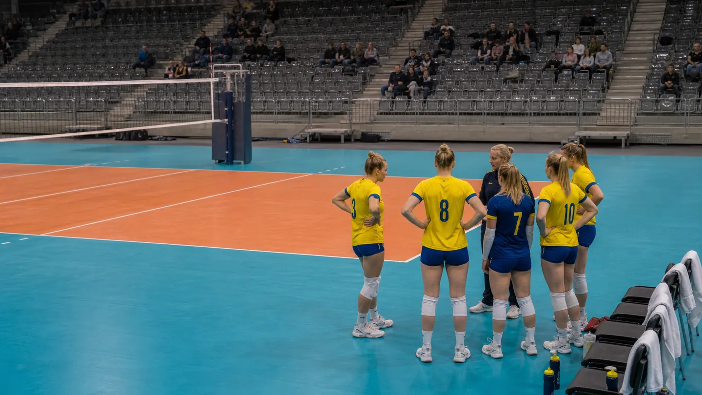 Damspelare i gula och blå volleybolldräkter samlade vid bänken under en timeout.